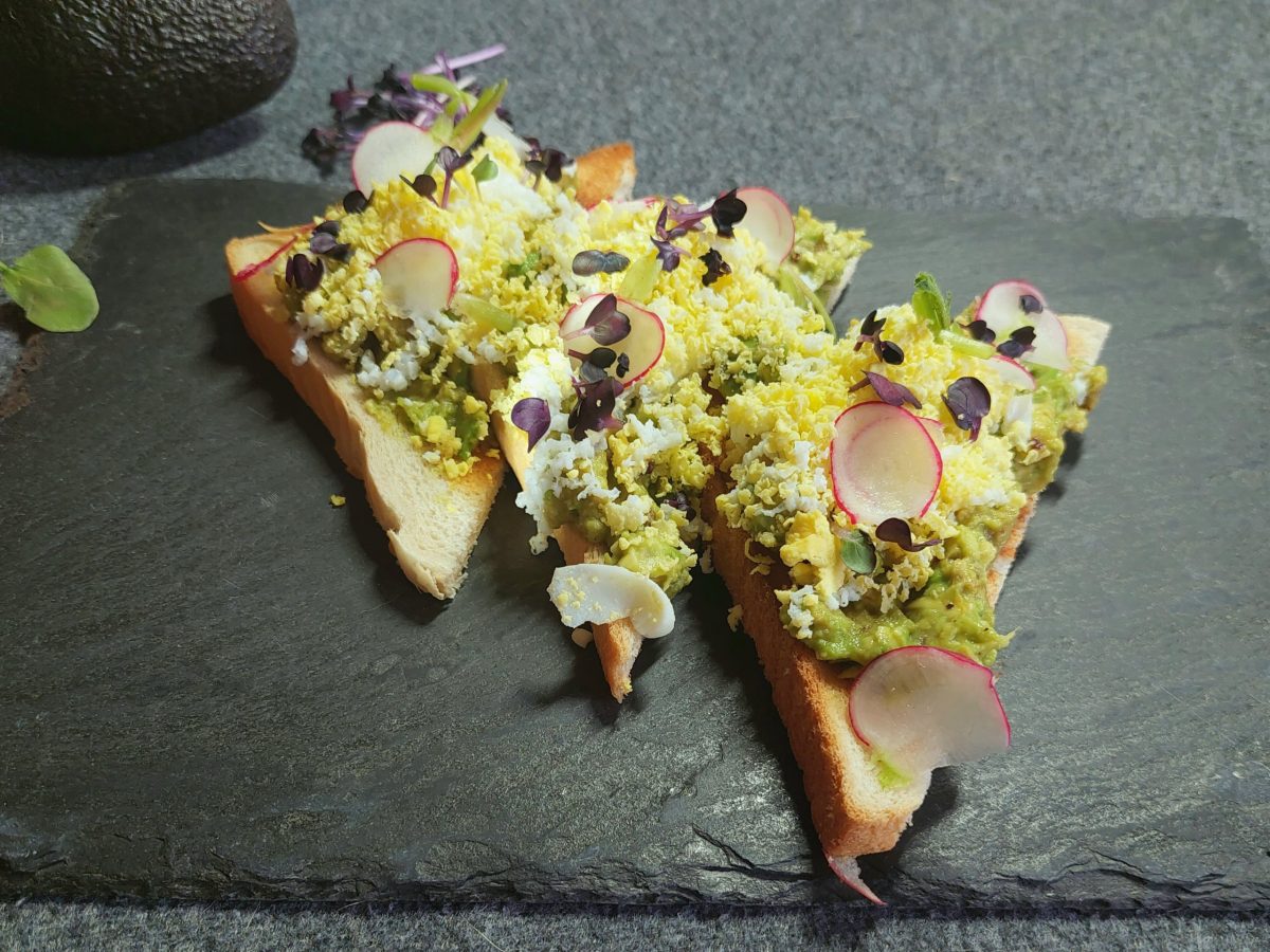 Avocado-Toast von oben mit geriebenem Ei auf schwarzer Schieferplatte