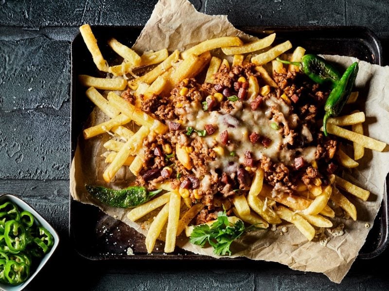 Ein Backblech vegane Chili Cheese Fries mit frischer Petersilie in der Draufsicht.