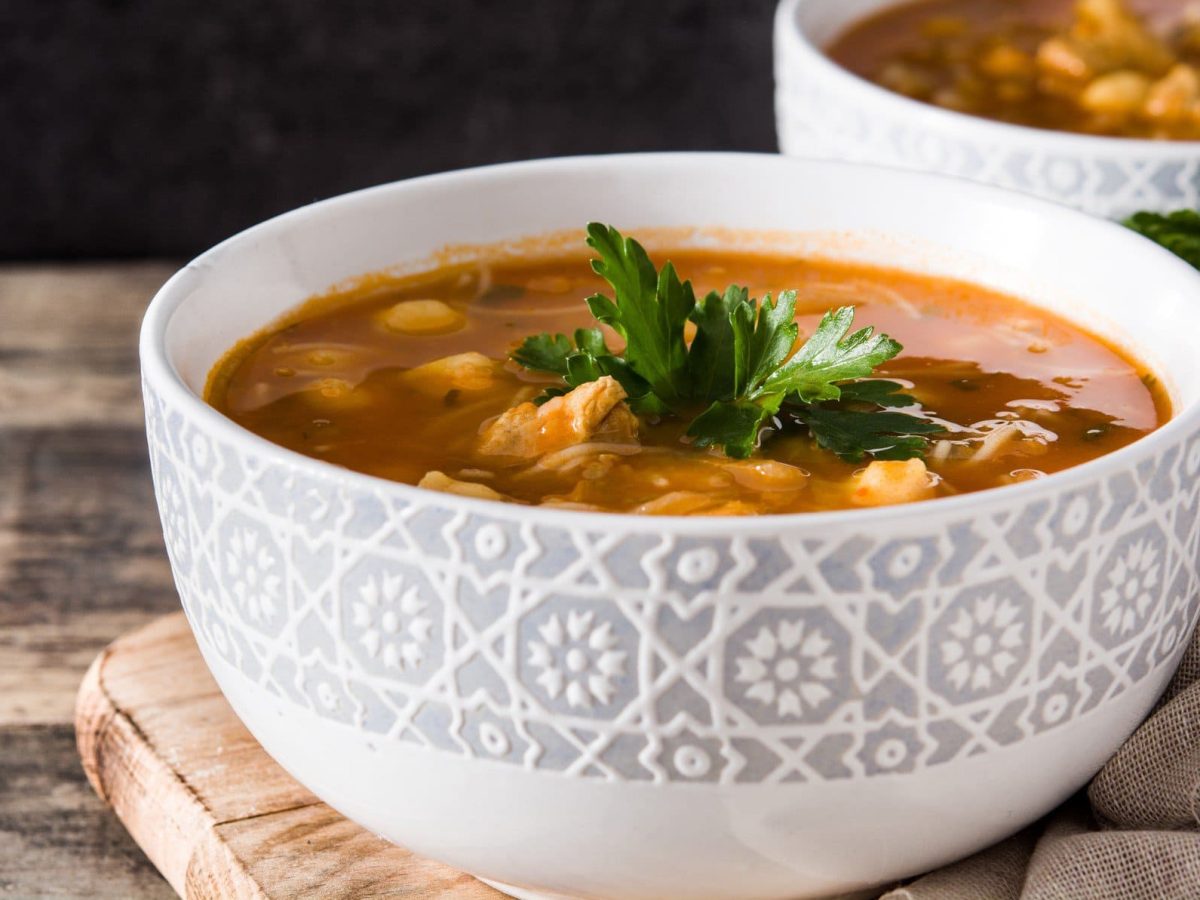 Zwei Schüsseln mit veganer marokkanischer Harira-Suppe, eine rote Suppe mit Kichererbsen und Tomaten, mit Petersilie garniert.