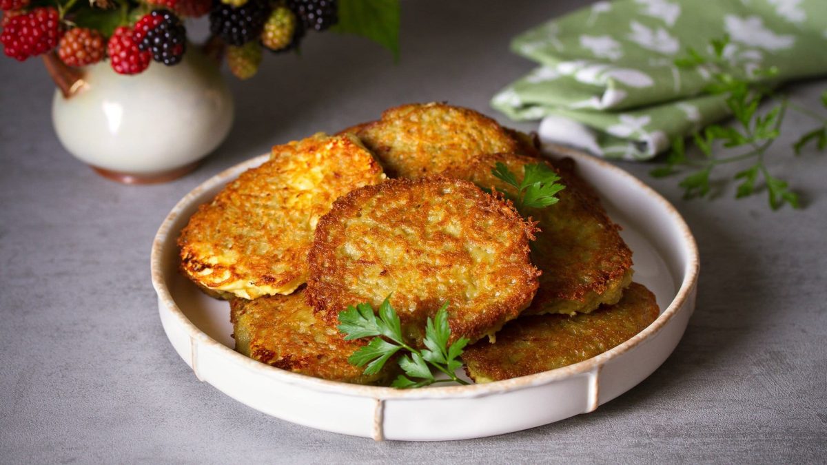 Ein Teller vegane Süßkartoffelpuffer mit Petersilie, dahinter ein Geschirrhandtuch.