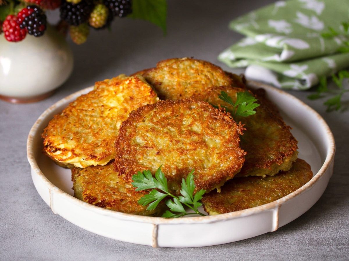 Ein Teller vegane Süßkartoffelpuffer mit Petersilie, dahinter ein Geschirrhandtuch.