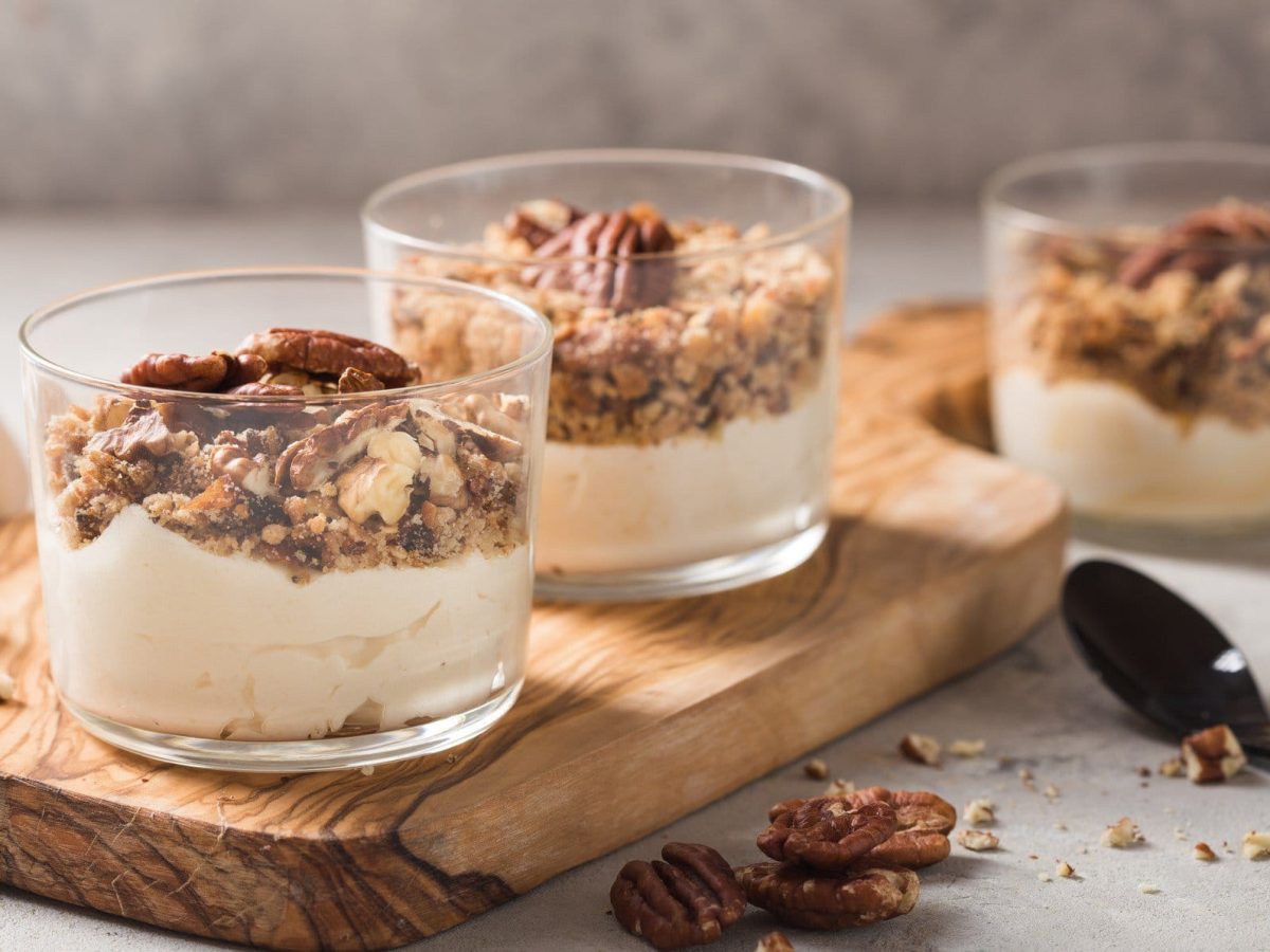 Drei Dessertgläser mit veganer Vanille-Mousse und Müsli auf einem Holzbrett.