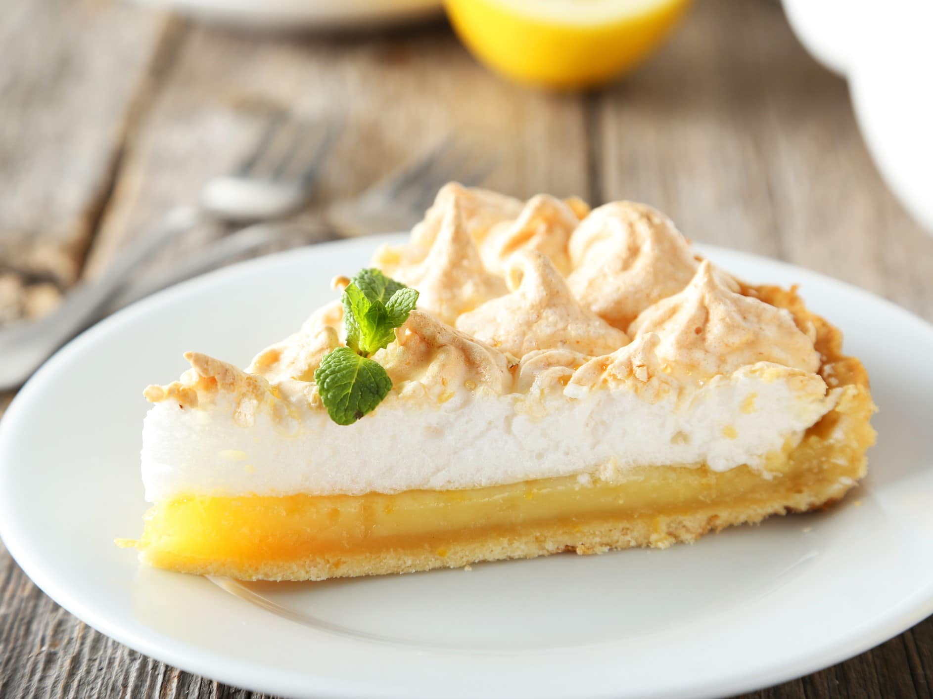 Limoncello-Tarte mit Baiserhaube auf einem weißen Teller. Das Ganze auf einem hölzernen Untergrund.