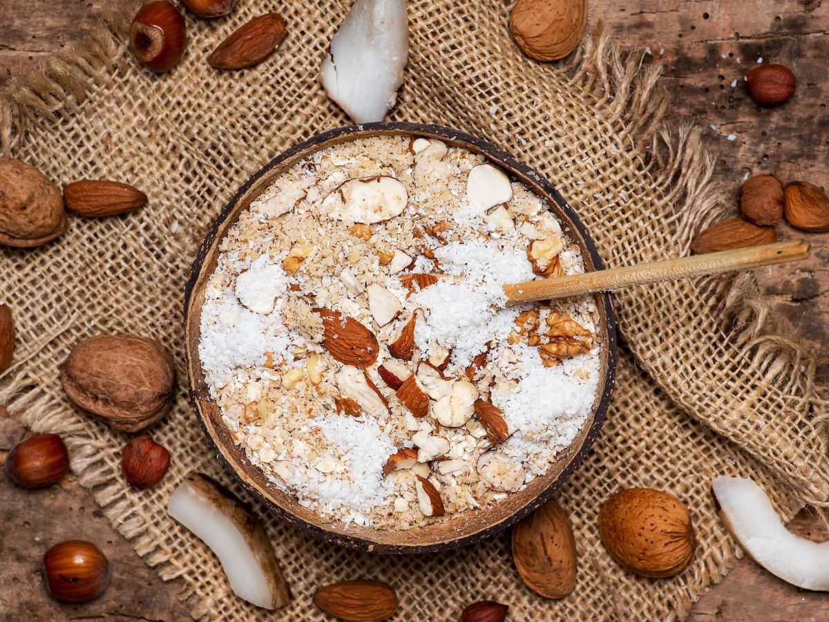 Würziger Nuss-Porridge mit frischem Ingwer, Kokosflocken und Gewürzen in einer Schale auf einem Tisch aus Holz