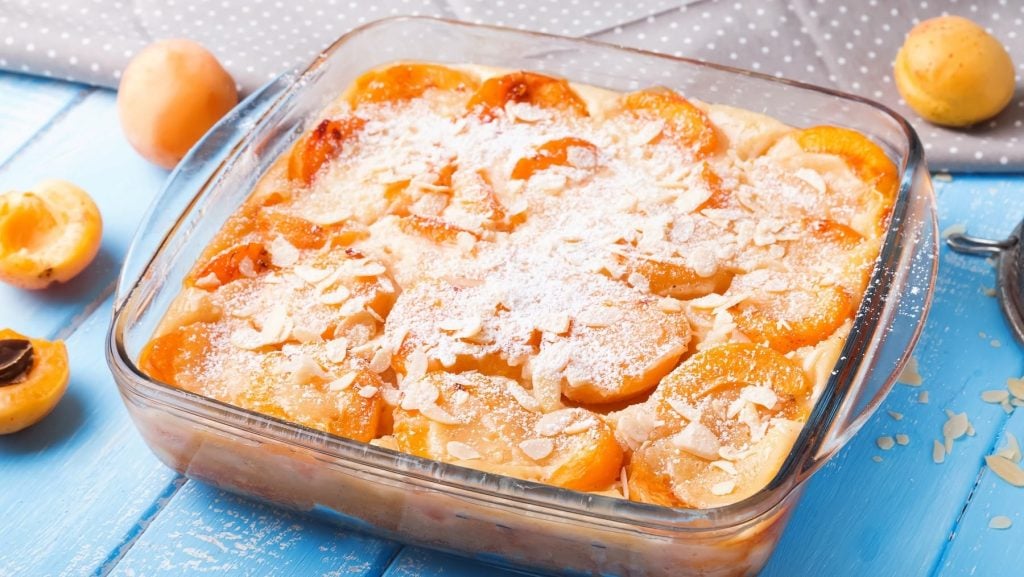 Saftiger Aprikosen-Clafoutis aus Pfannkuchen-Teig und fruchtigen Aprikosen, bestreut mit Mandlen und Puderzucker.