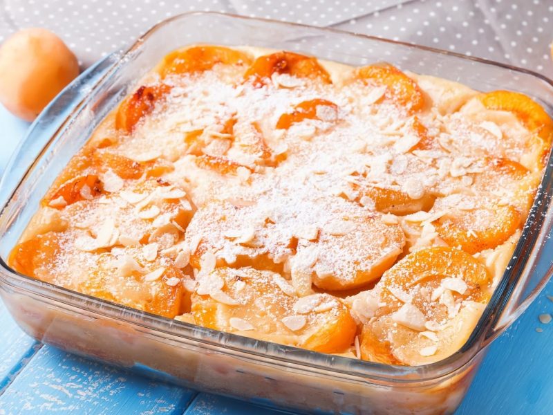 Saftiger Aprikosen-Clafoutis aus Pfannkuchen-Teig und fruchtigen Aprikosen, bestreut mit Mandlen und Puderzucker.