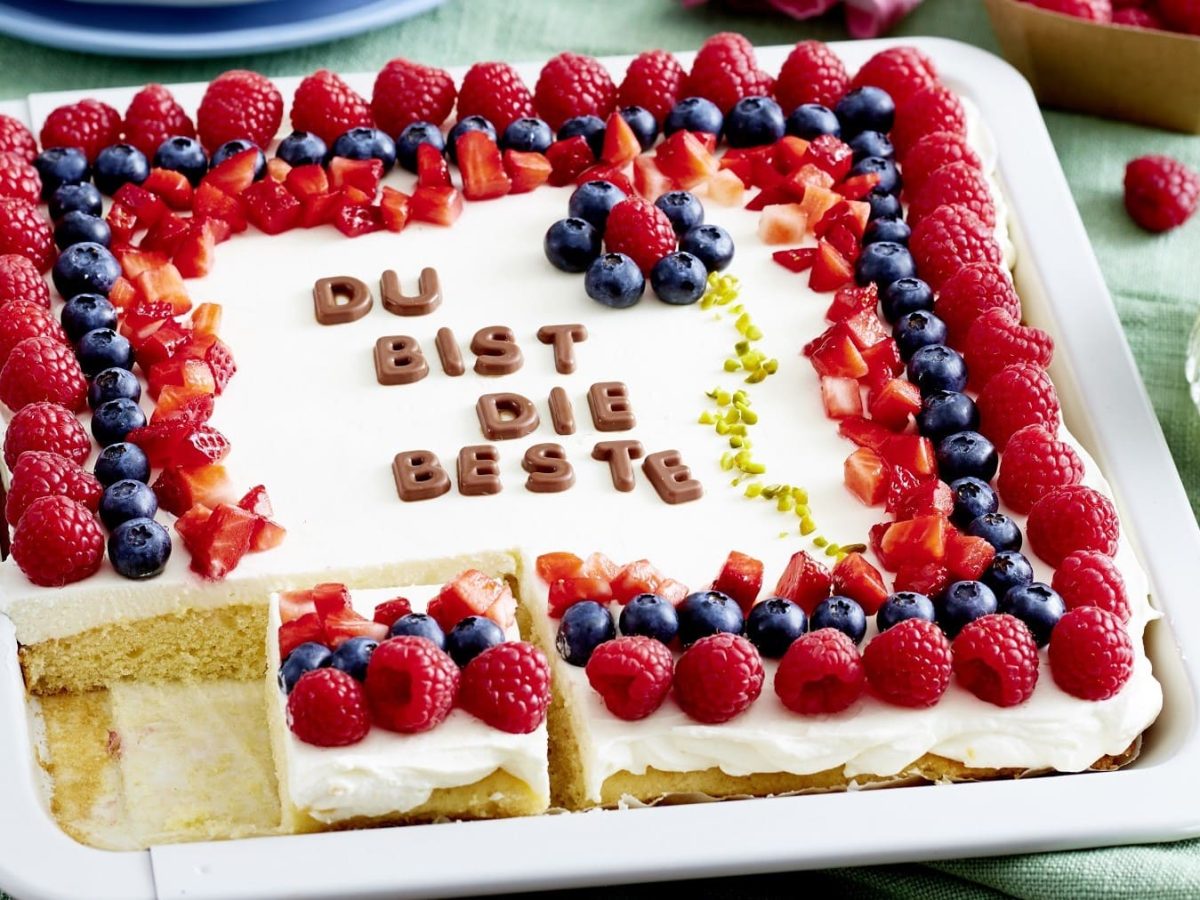 Auf einem Blech liegt ein Du-bist-die-Beste-Kuchen. Er ist dekoriert mit frischen Beeren und essbaren Buchstaben.