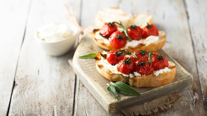 Bruschetta mit Grilltomate auf Holzbrett serviert.