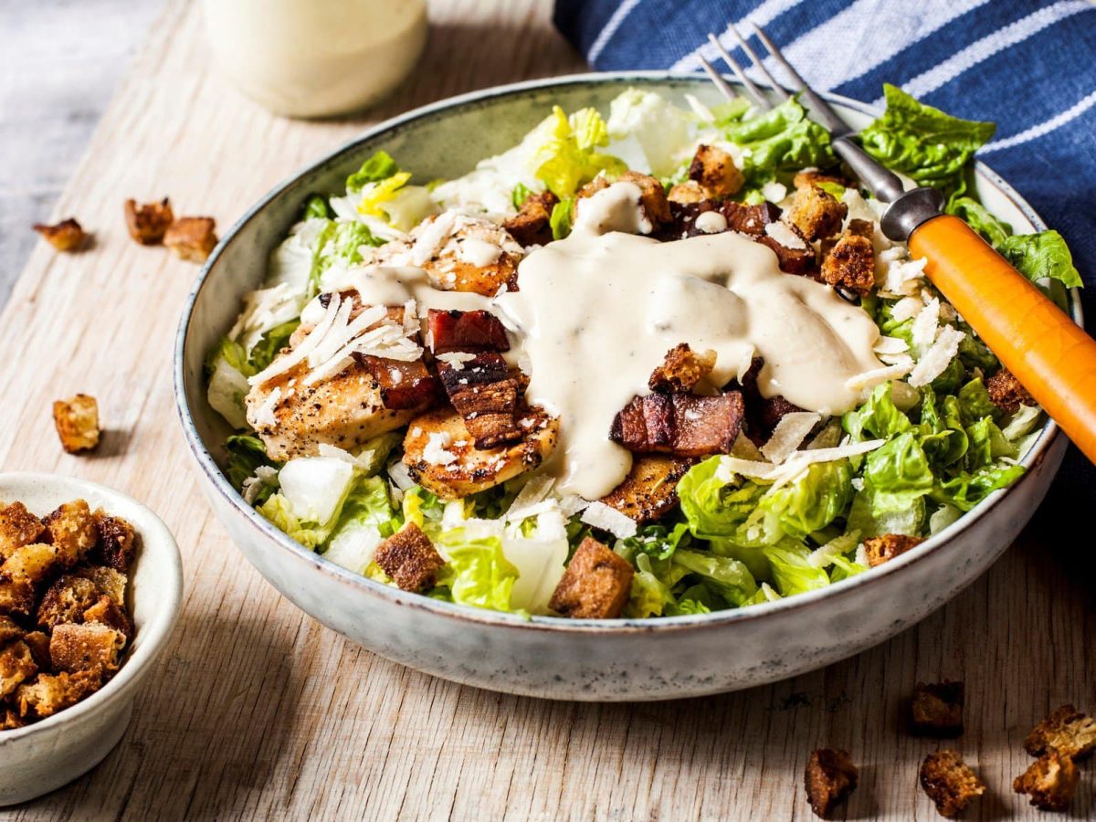 Schüssel mit Caesar Salat angerichtet auf einem Holzbrett.