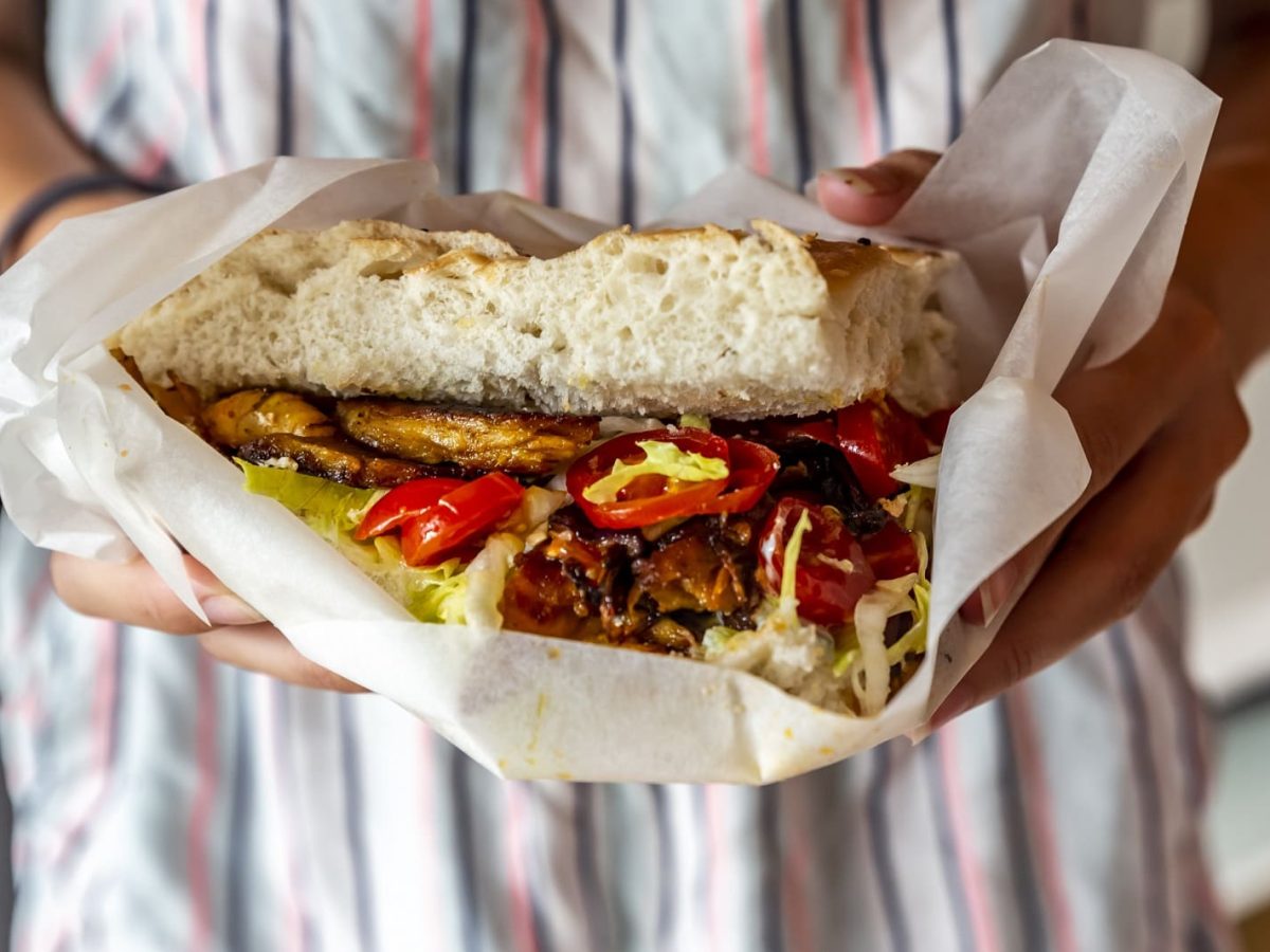 Eine mit gestreifter Schürze gekleidete Frau hält einen frischen Döner in die Kamera.