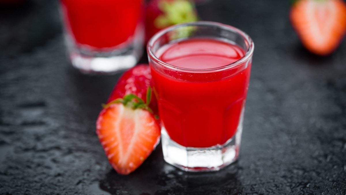 Ein Shot-Glas mit Erdbeerlimes auf Schiefer-Untergrund. Daneben liegen Erdbeeren.