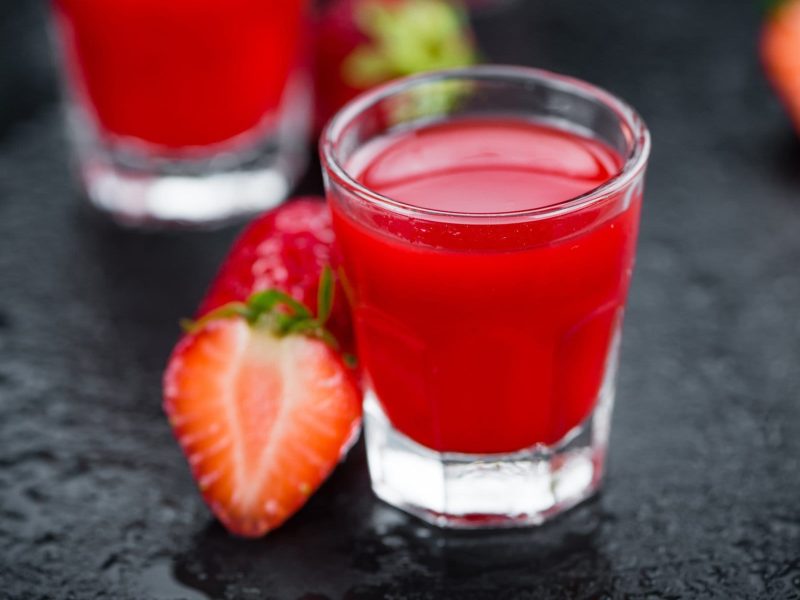 Ein Shot-Glas mit Erdbeerlimes auf Schiefer-Untergrund. Daneben liegen Erdbeeren.