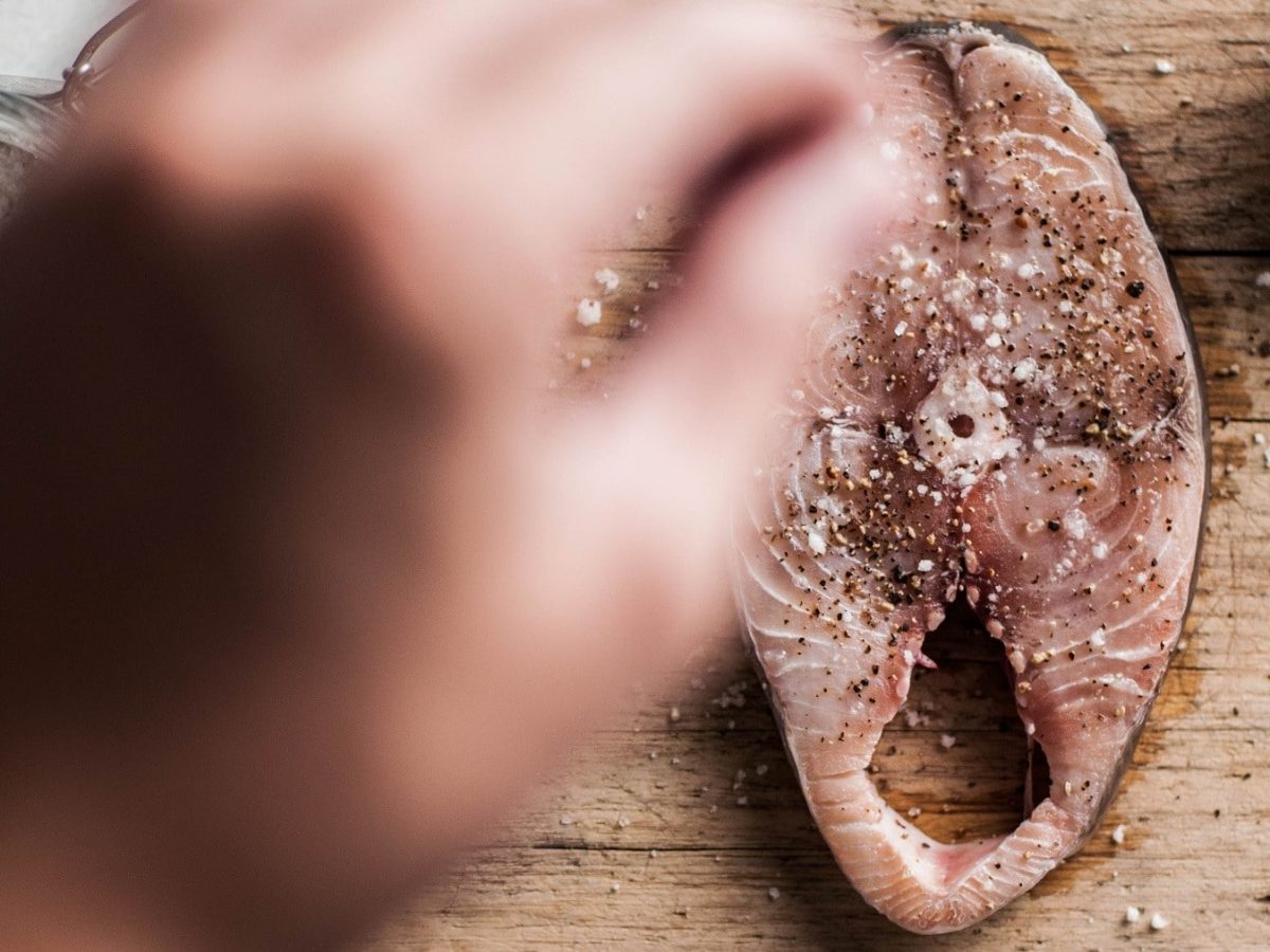 Selbst gemachtes Fisch-Gewürz wird von einer Hand auf ein Stück Makrelen-Steak gestreut.