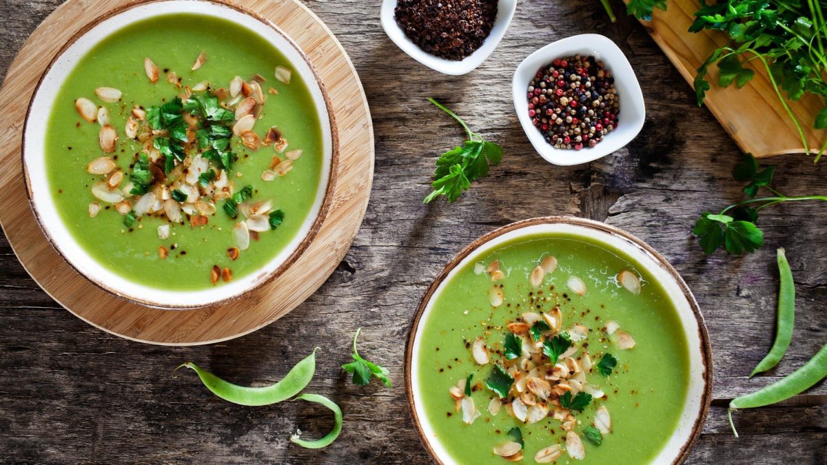 Zwei Teller gefüllt mit einer grünen Gemüsesuppe und dekoriert mit gerösteten Mandeln und Kräutern.