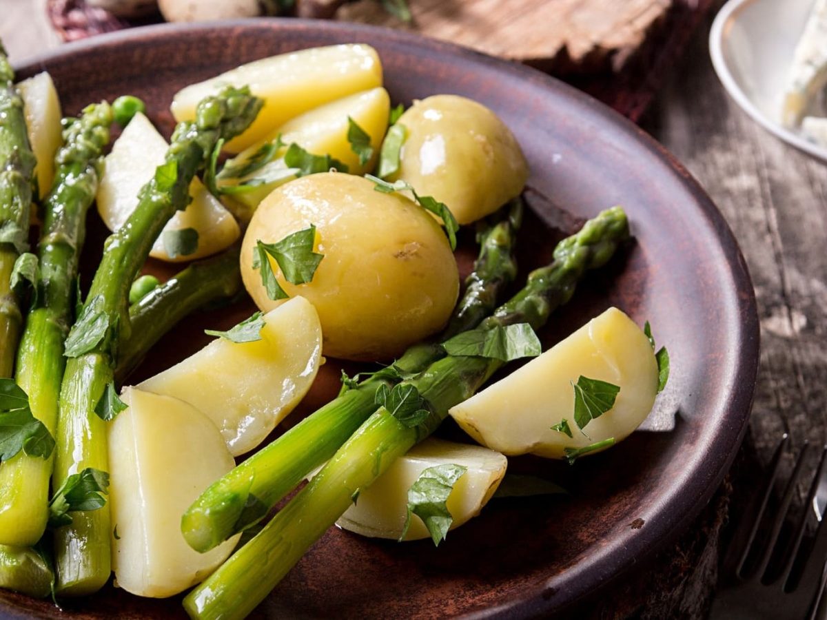 Grüner Spargel mit Kartoffeln auf Teller serviert.