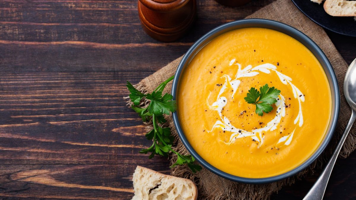 Dunkle Schüssel gefüllt mit Möhren-Ingwer-Suppe auf hölzernem Untergrund.