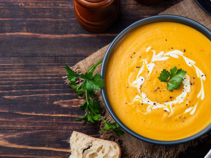 Dunkle Schüssel gefüllt mit Möhren-Ingwer-Suppe auf hölzernem Untergrund.