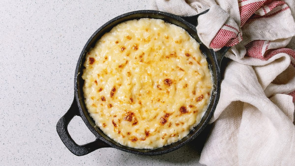 Schwarze gusseiserne Form gefüllt mit Käse-Makkaroni auf weißem Untergrund.