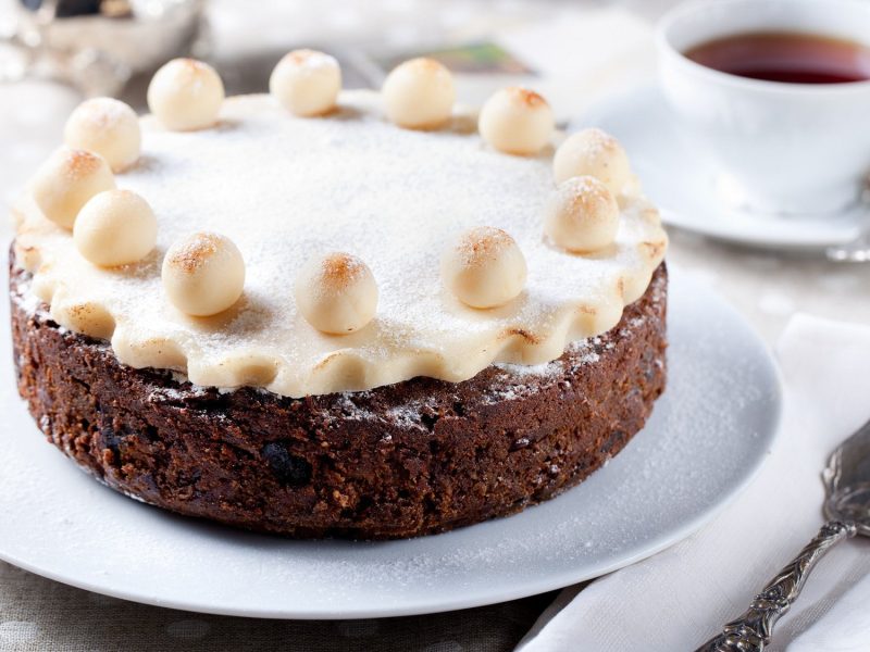 Simnel Cake auf einem weißen Teller. Daneben steht eine Tasse Tee.