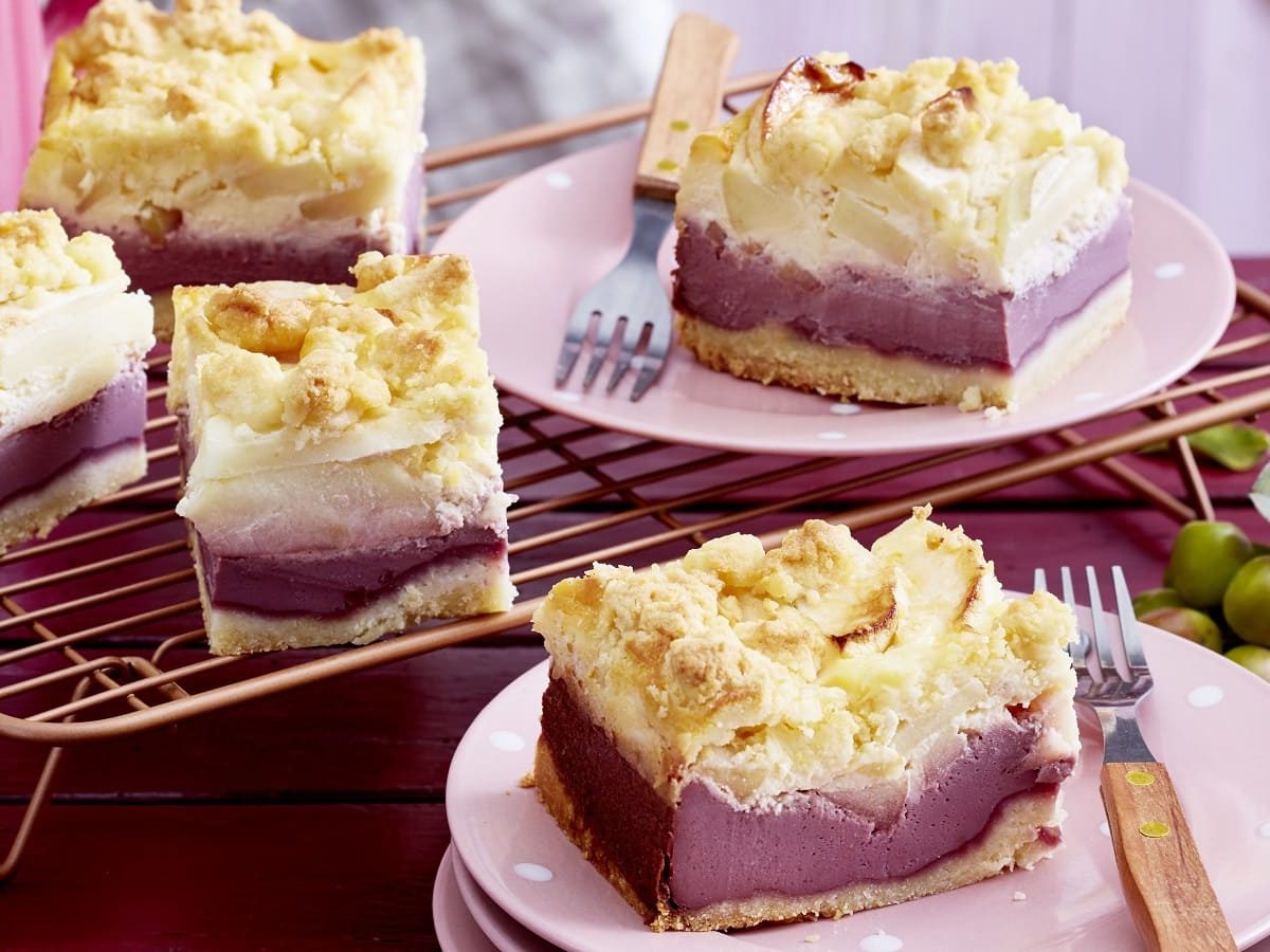 Apfelholunder-Streuselkuchen auf einem rosa Teller neben einer Gabel auf einem gedeckten Tisch