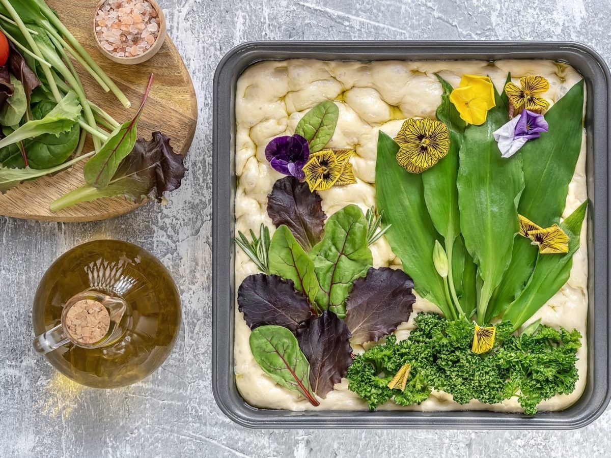 Eine Bärlauch-Focaccia vor dem Backen, ihr Belag ist als Blumenwiese belegt.