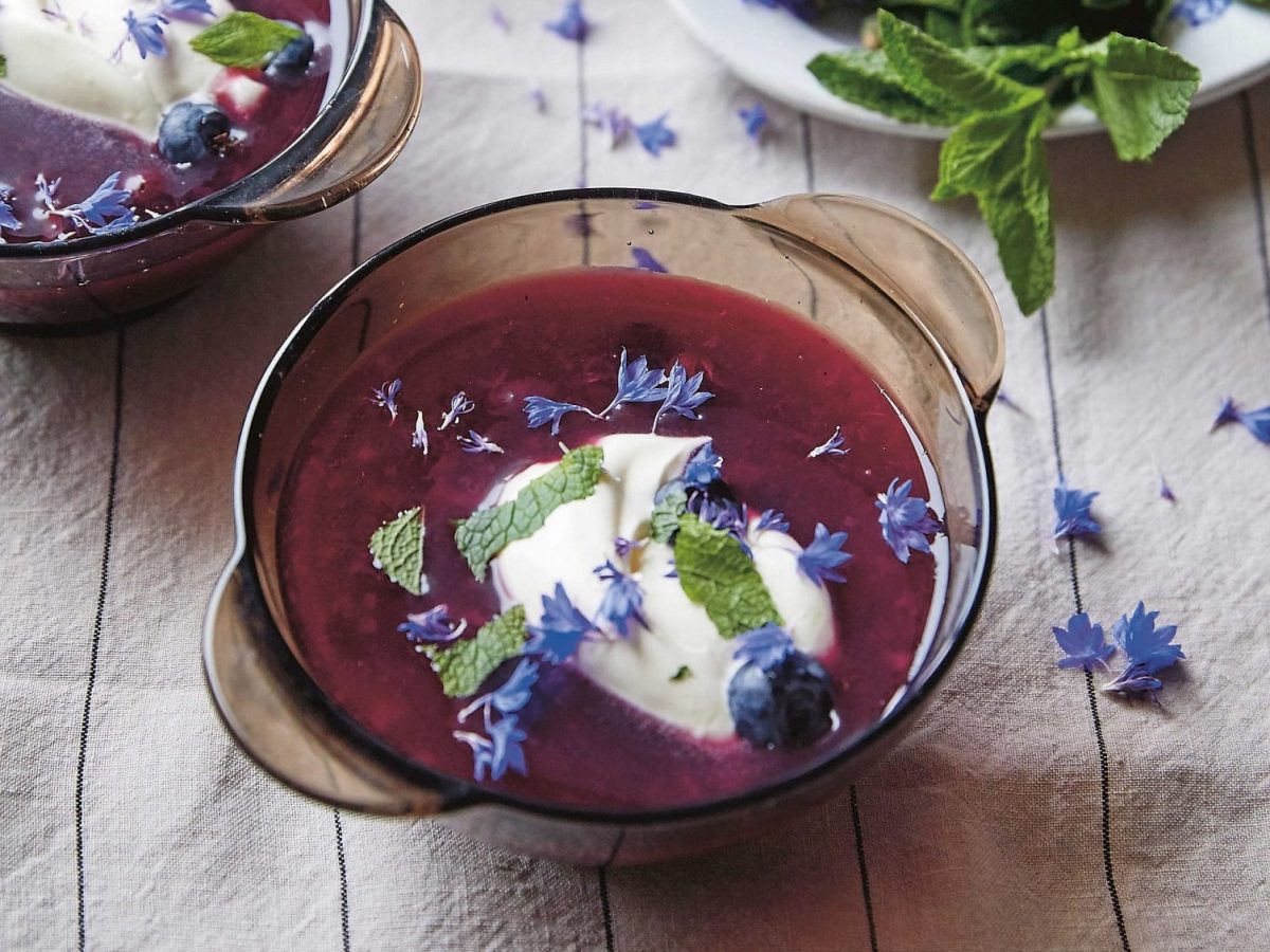 Zwei Glasschalen mit Heidelbeersuppe, Minze, Joghurt und Blüten auf einem Geschirrtuch, ein Rezept aus dem Kochbuch "Baltikum".