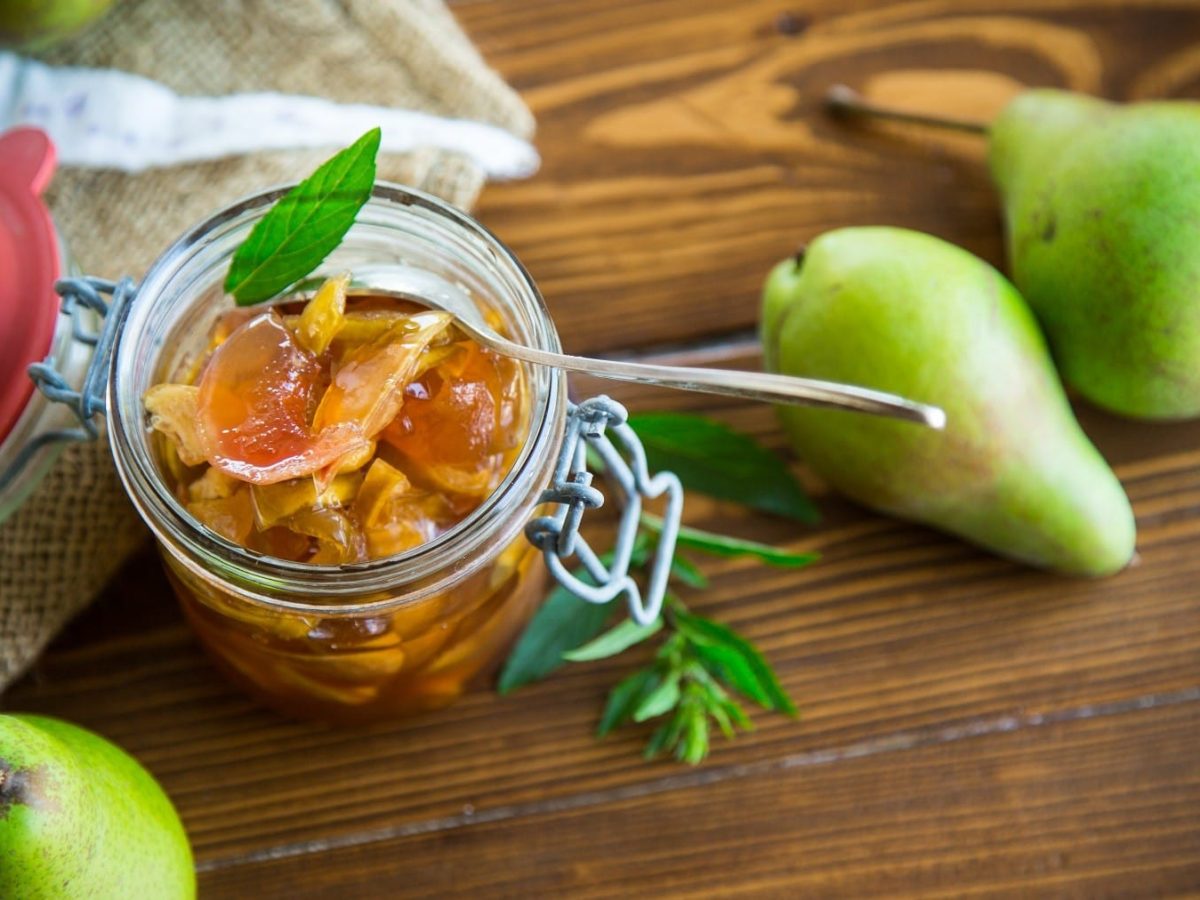 Birnen-Chutney geöffnet in einem Einweckglas, garniert mit Kräutern auf einem Holztisch, umgeben von ganzen frischen Birnen