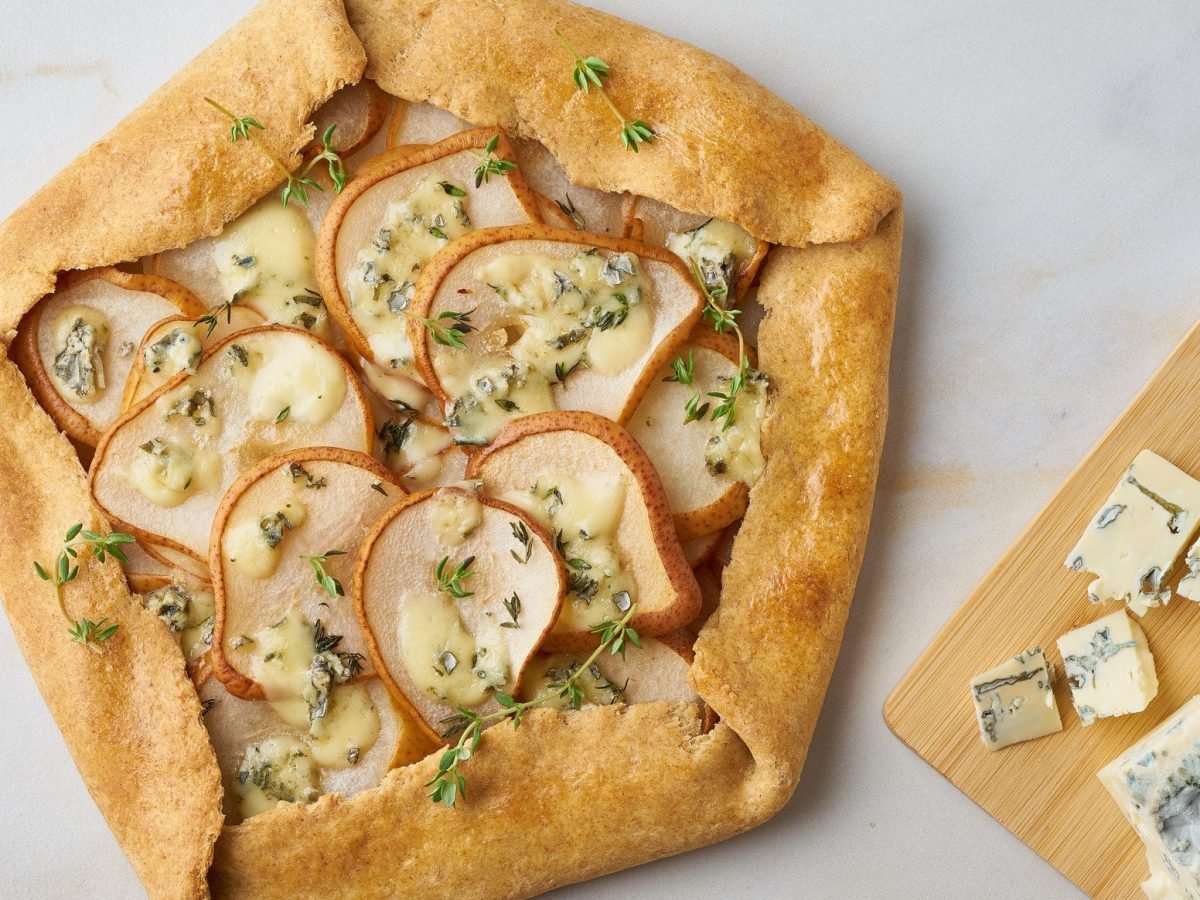 Birnen Galette mit Gorgonzola auf einem weißen Untergrund. Daneben ein Holzbrett mit Gorgonzola.