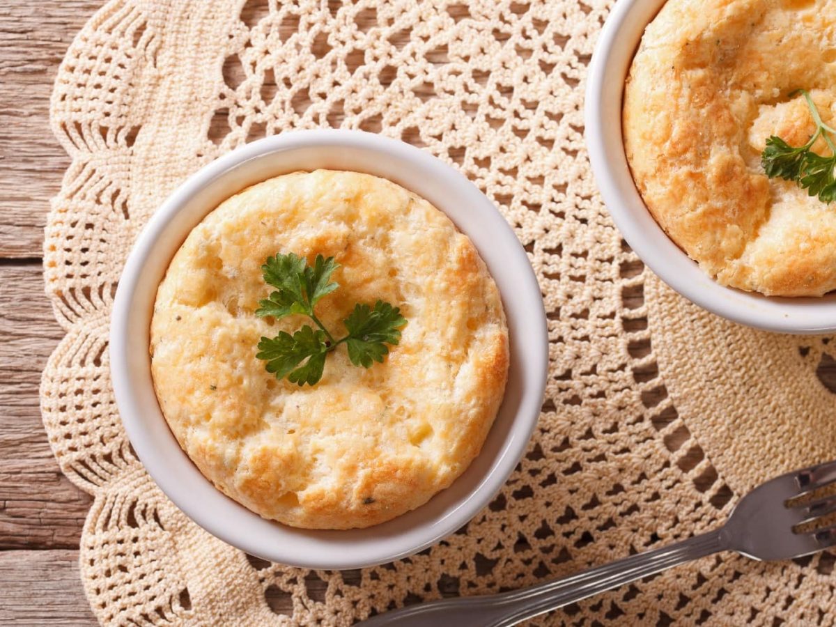 Zwei Cheddar-Souffles auf einem Holztisch mit beiger Tischdecke in Horizontalansicht von oben.