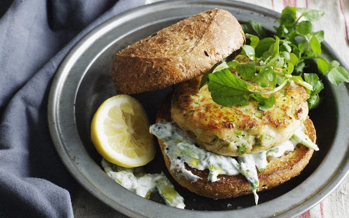 Saftiger Forellen-Burger-Patty auf einem klassischen Brötchen mit Tzaziki, garniert mit wildem Salat.