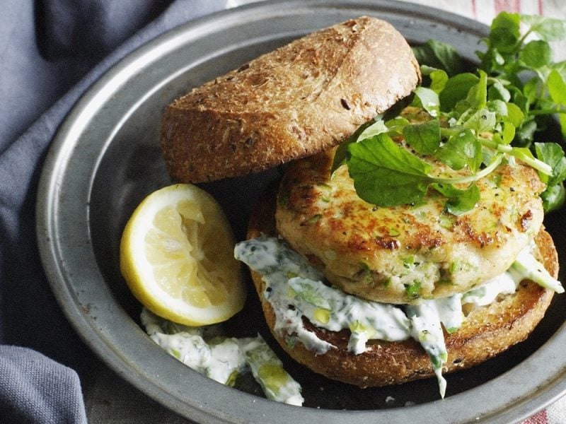 Saftiger Forellen-Burger-Patty auf einem klassischen Brötchen mit Tzaziki, garniert mit wildem Salat.