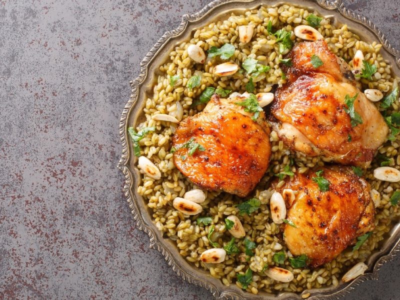 Libanesisches Freekeh mit Hähnchen auf einem Teller auf grauem Stein-Untergrund