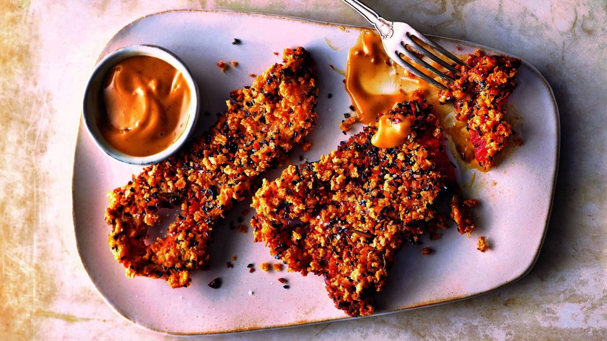 Ein Teller frittierte Spitzpaprika mit einem Schälchen, in dem ein gelber Dip ist. Draufsicht.