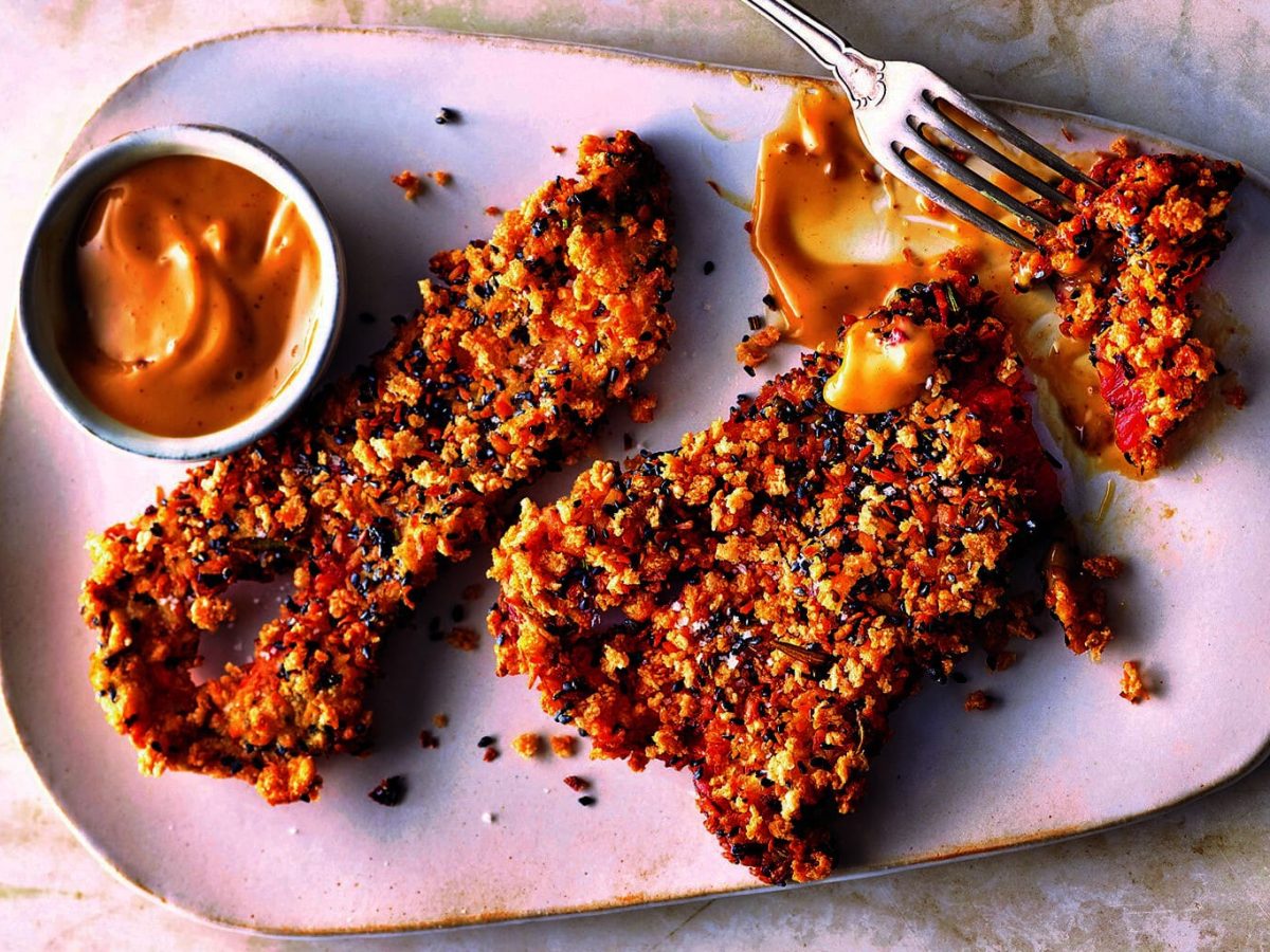 Ein Teller frittierte Spitzpaprika mit einem Schälchen, in dem ein gelber Dip ist. Draufsicht.