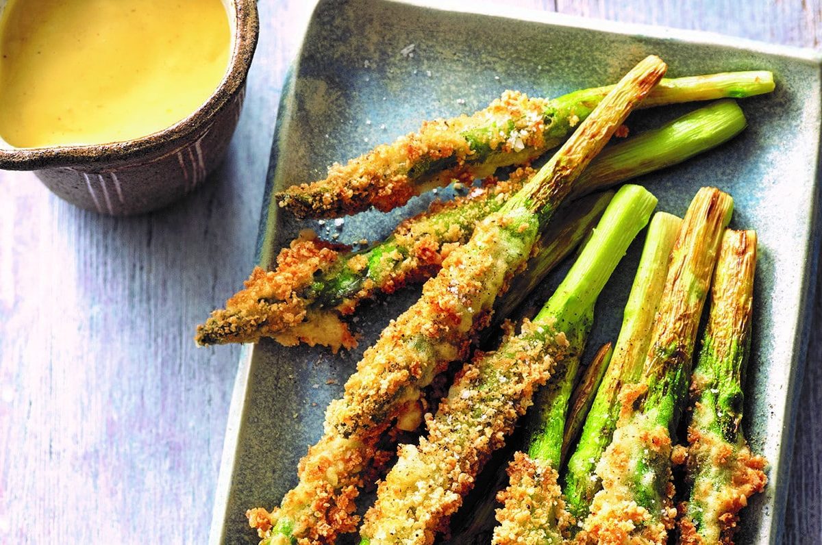 Frittierter grüner Spargel mit japanischer Sauce hollandaise, die in einem Kännchen daneben steht. Draufsicht.