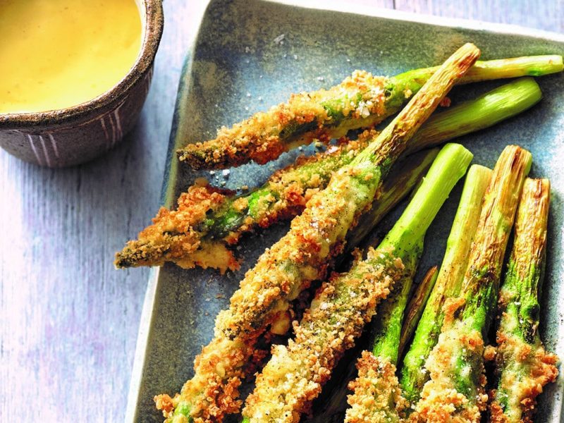 Frittierter grüner Spargel mit japanischer Sauce hollandaise, die in einem Kännchen daneben steht. Draufsicht.