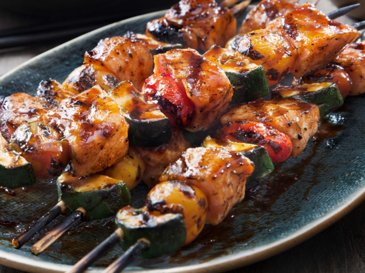 Gegrillte Lachsspieße mit Teriyaki-Basting, Tomaten und Gemüse auf blauem Teller auf Holztisch. Aufnahme aus der Vogelperspektive.