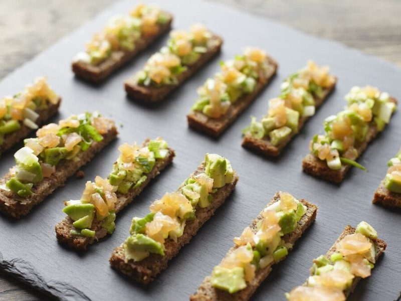 Auf einem Schieferbrettchen liegen Guacamole-Lachs-Stangen