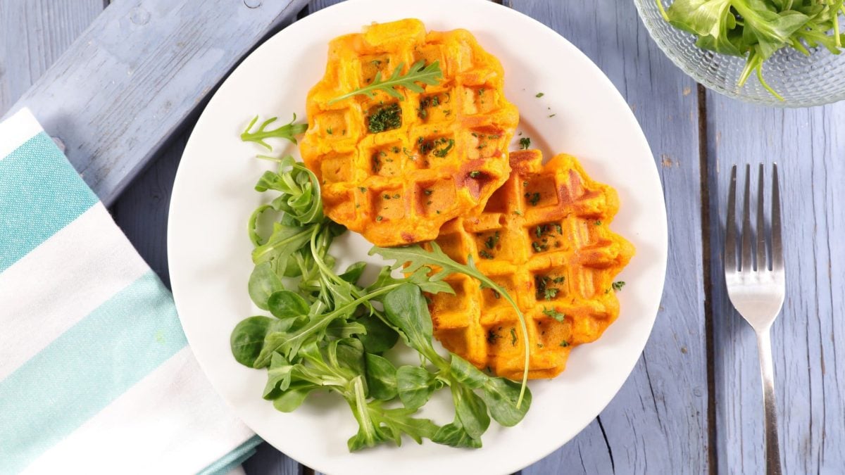 Herzhafte Süßkartoffelwaffeln mit Chili mit grünem Salat auf einem Teller in der Draufsicht, daneben liegen eine Gabel und eine Stoffserviette.