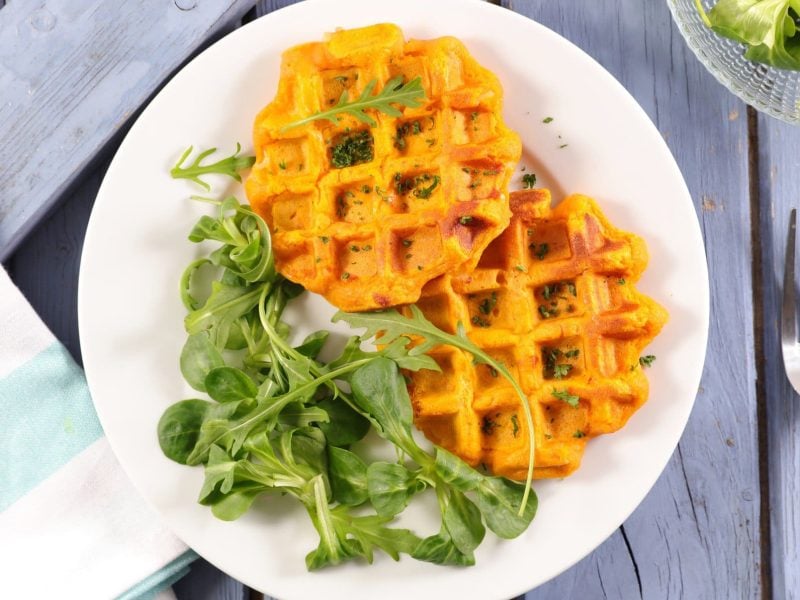 Herzhafte Süßkartoffelwaffeln mit Chili mit grünem Salat auf einem Teller in der Draufsicht, daneben liegen eine Gabel und eine Stoffserviette.