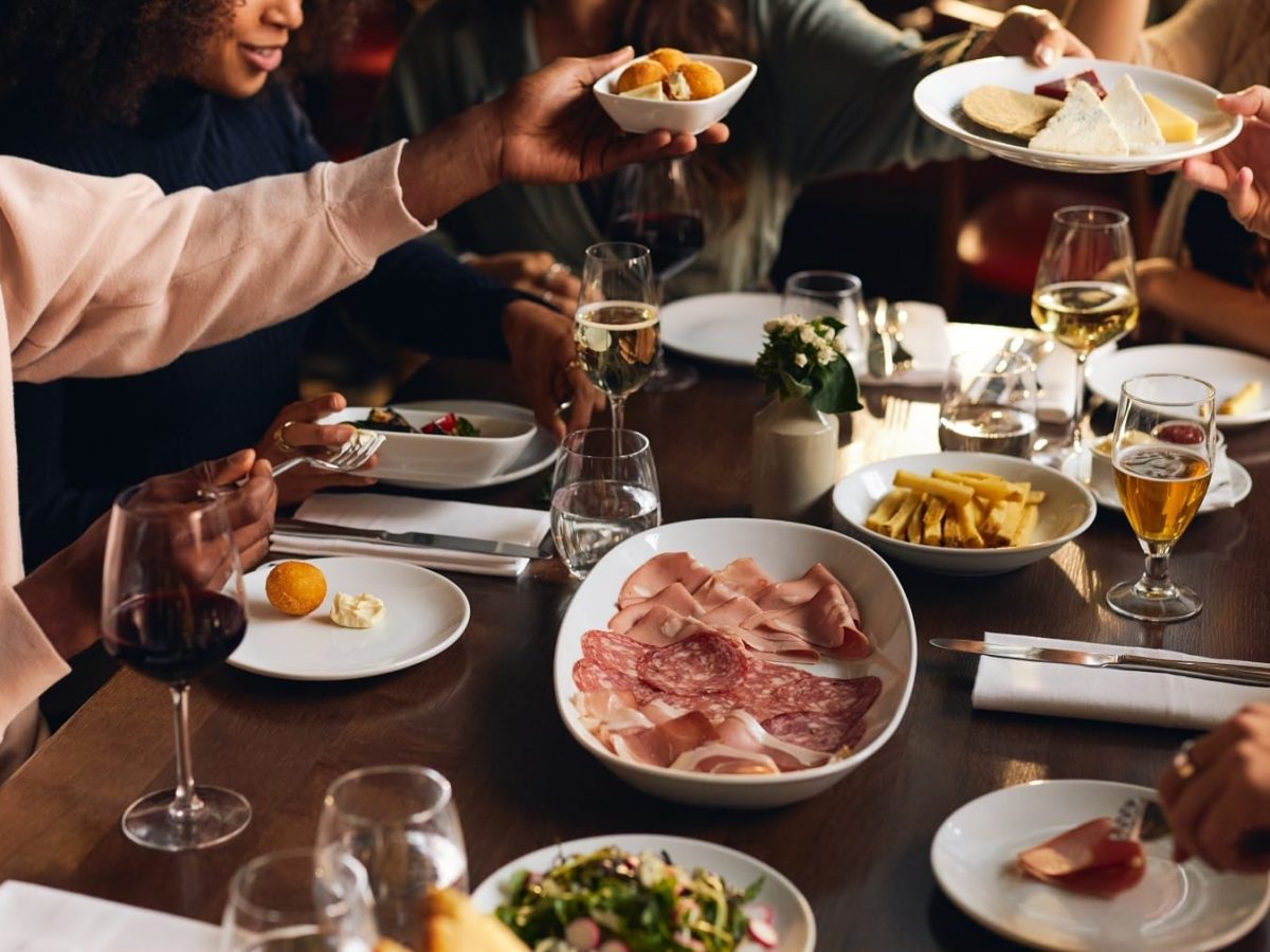 Italienisches Menü, begonnen mit verschiedenen Antipasti auf einem Tisch. Die einzelnen Speisen werden von den Menschen herumgereicht.