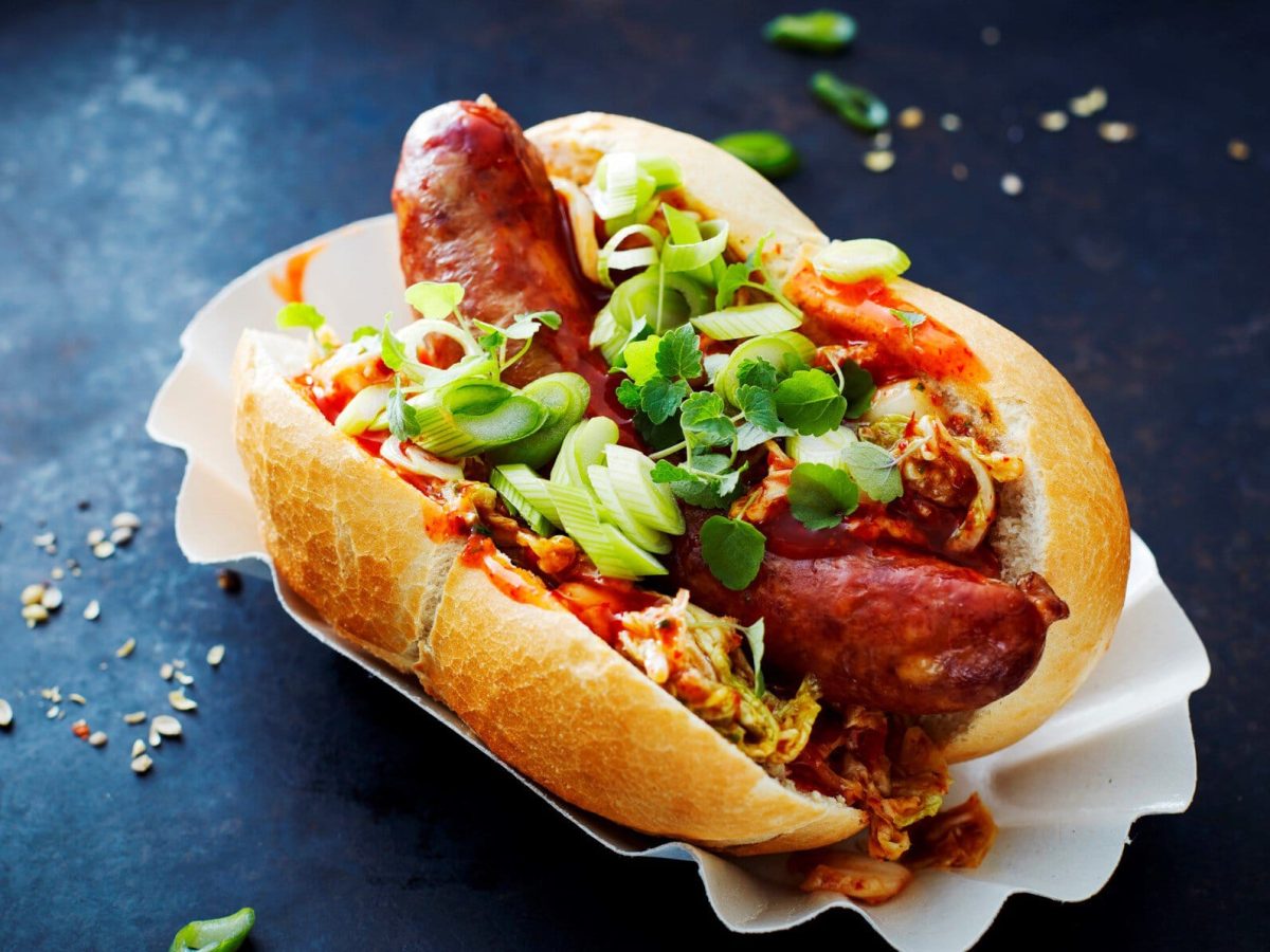 Schräge Aufnahme vom Kimchi-Hot-Dog auf einer weißen Schale und dunklem Untergrund.