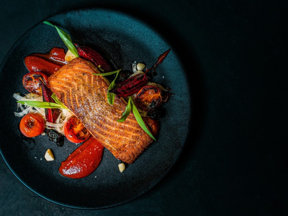 Draufsicht auf einen blauen Teller mit Lachs auf Fenchelsalat. Garniert mit roter Bete und Kirschtomaten.