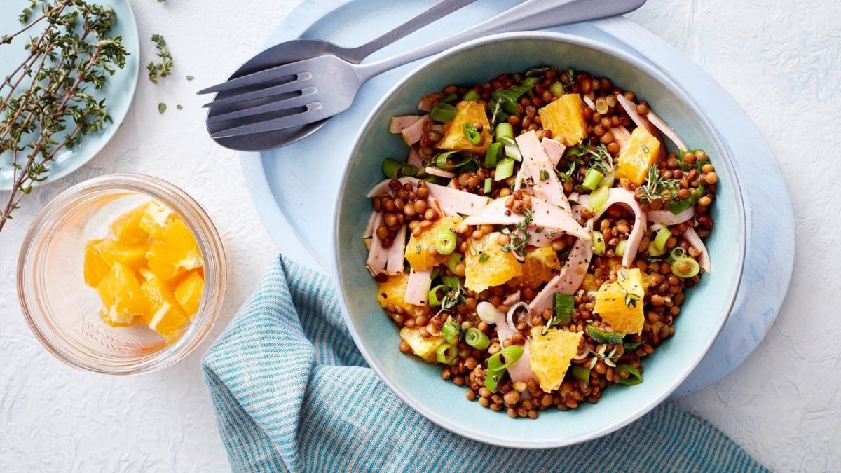 Linsensalat mit Fruchtnote, garniert mit frischem Thymian, feiner Vinaigrette und Kasseler-Streifen in einer hellen Schale auf weißem Untergrund