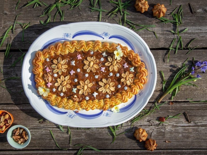 Klassischer polnischer Mazurek-Kuchen, bestehend aus Mürbeteig, einem gespritzen Rand, Marmelade, und feinen Dekor aus Nüssen und weiteren Zuckereien auf einem hölzernen Tisch.