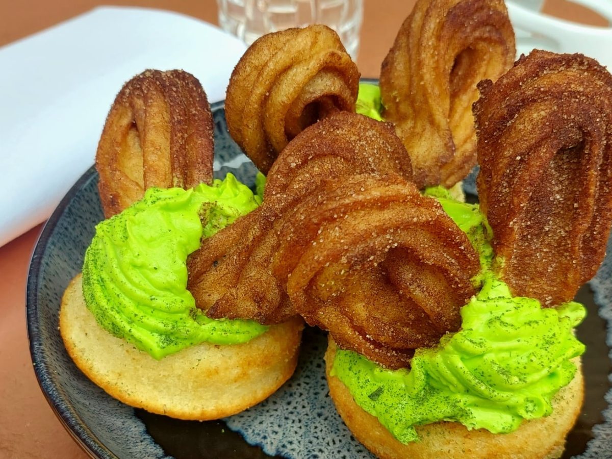 Cupcakes mit grüner Creme und Hasenohren aus Churros auf blauem Teller und Bronze-Untergrund.