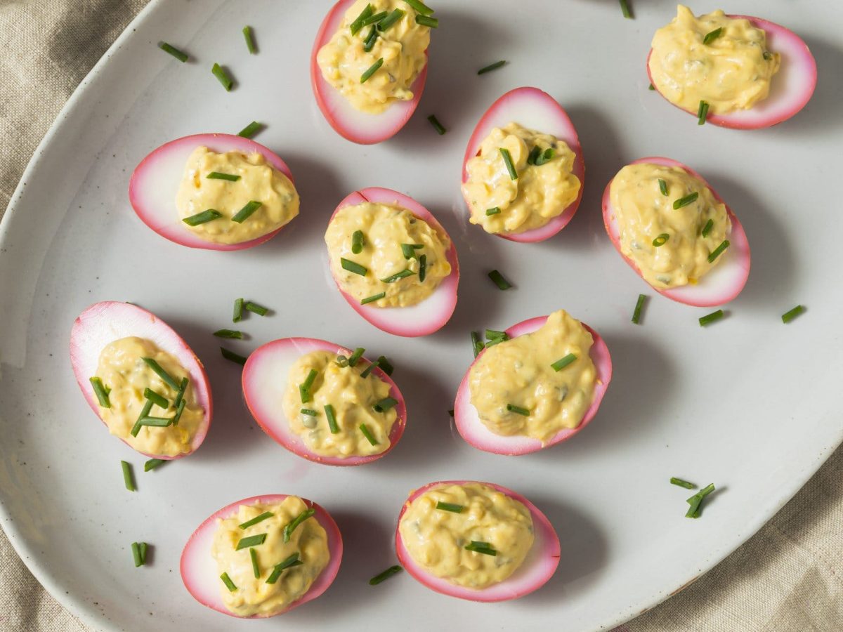 Pink deviled Eggs auf einem weißen Teller. Der Teller steht auf einem beigen Leinentuch.