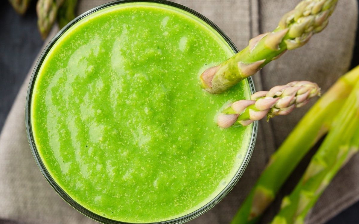 Grüner Spargel-Smoothie in einem Glas, garniert mit zwei grünen Spargel-Stangen auf einem hölzernen Tisch.