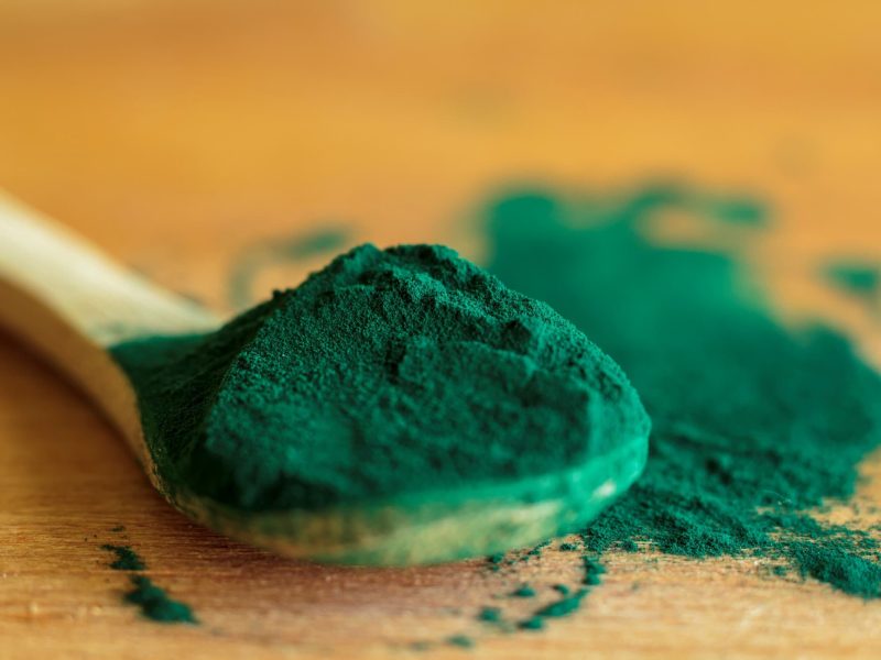 Ein Holzlöffel mit Spirulina-Pulver auf einem Holztisch.