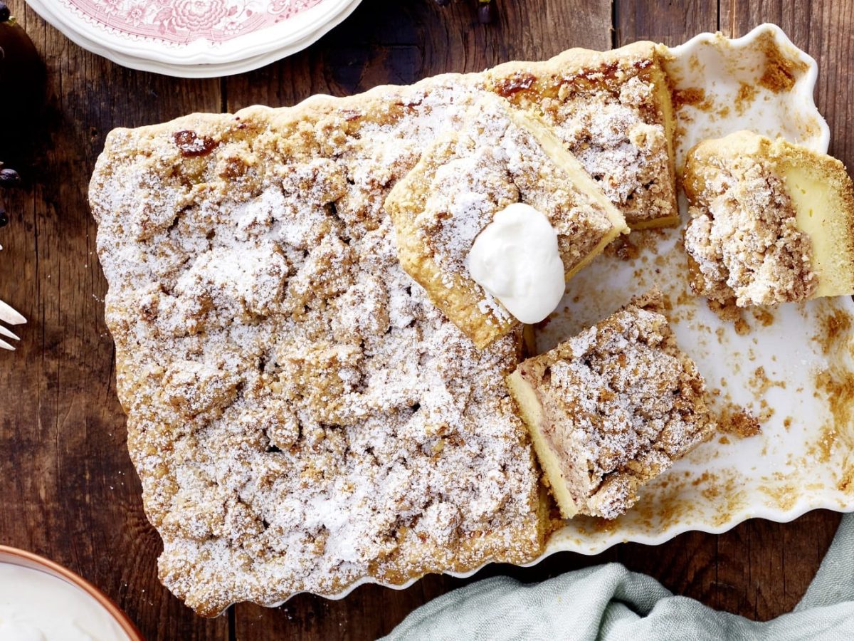 Streusel-Pudding-Tarte in einer weißen Form auf hölzernem Tisch, bestreut mit Puderzucker.